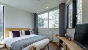 A modern bedroom with a large bed, a TV, and a window with a view of trees.