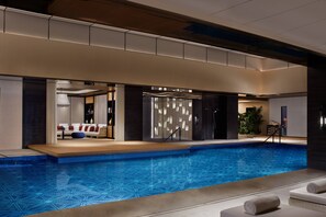 A modern indoor swimming pool with a geometric tile pattern, a lounge area with seating, and a reception desk.