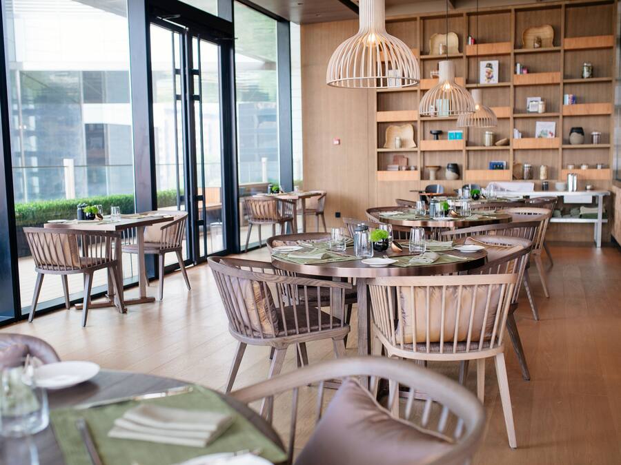 Ein Restaurant mit runden Tischen, Holzsesseln und hängenden Pendelleuchten.