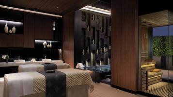 Relax in a serene spa room with two massage tables, a reception desk, and a glass partition offering a view of the outdoors.