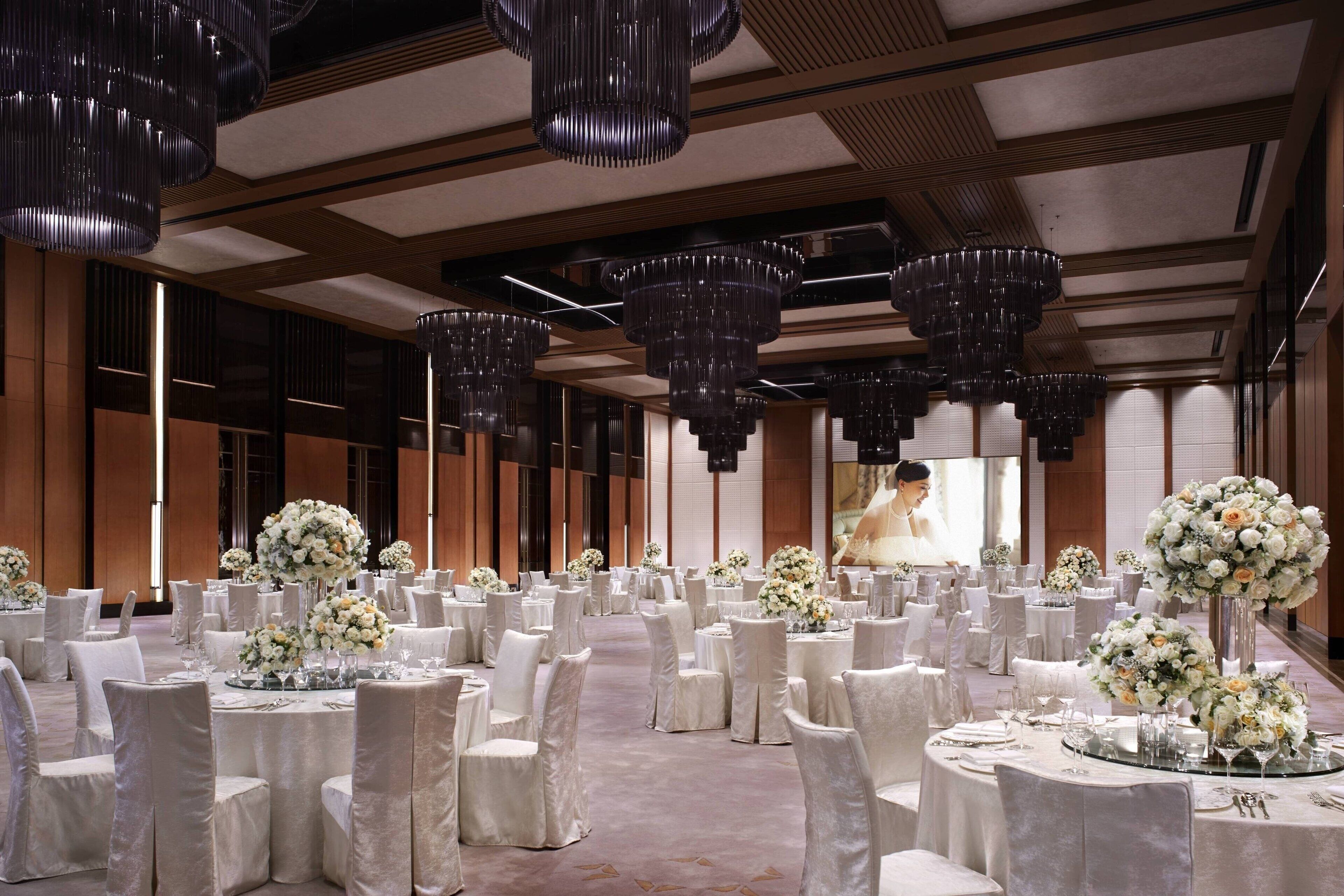 Un salón de banquetes con mesas redondas, sillas blancas y centros de mesa florales.