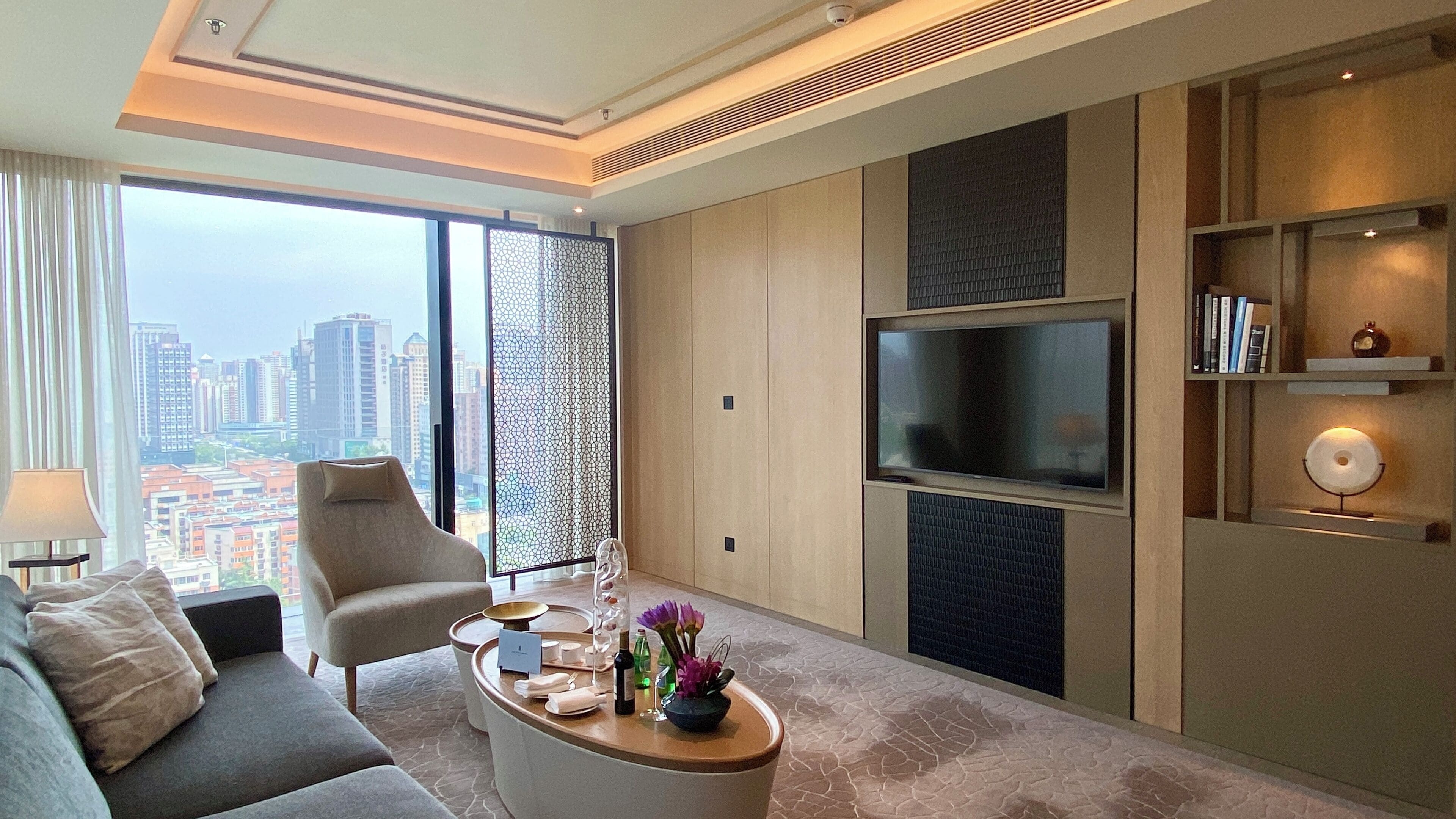 A modern living room with a sofa, armchair, coffee table, TV, and city view.