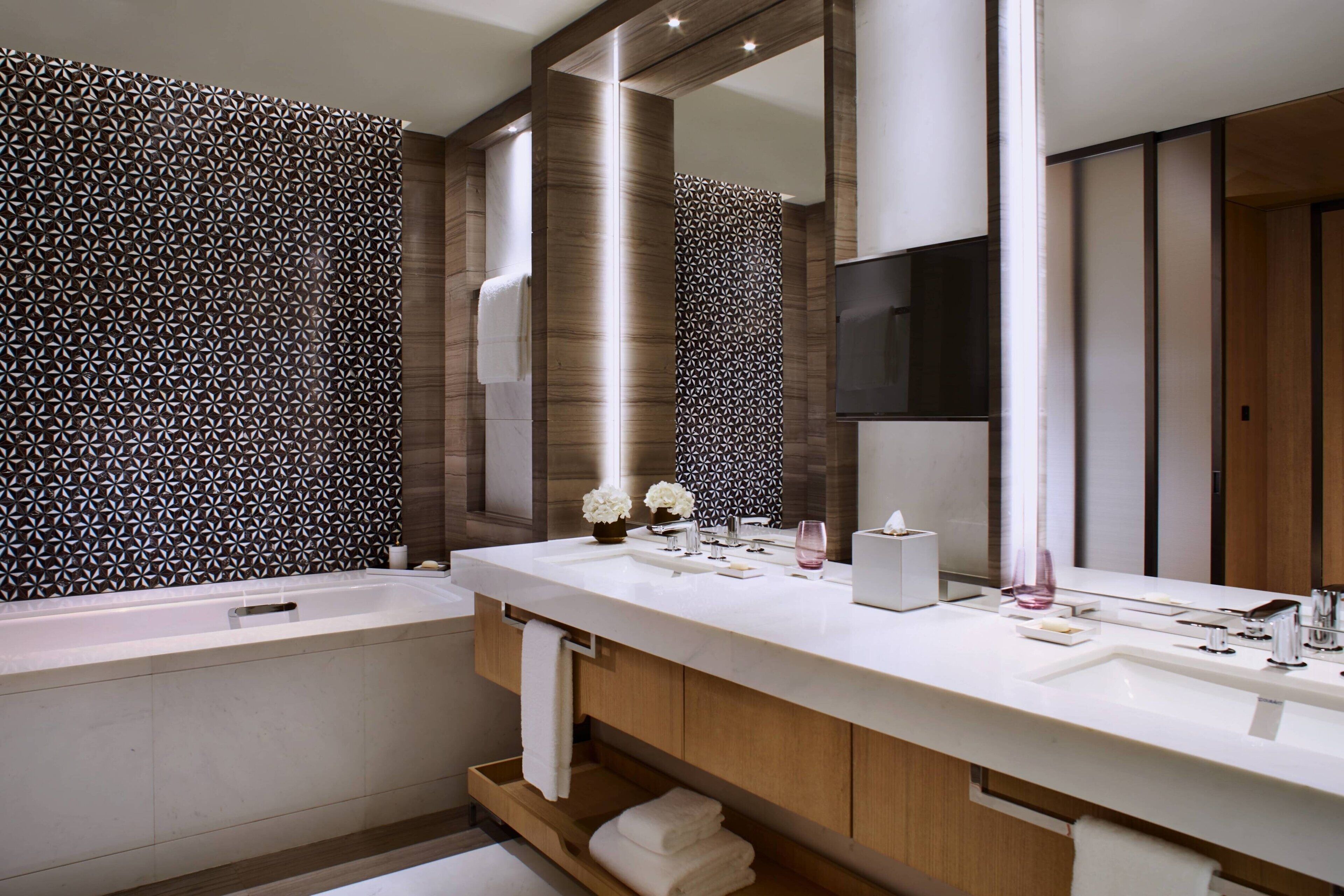 A modern bathroom with a large mirror, a bathtub, and a vanity with a sink and towel rack.