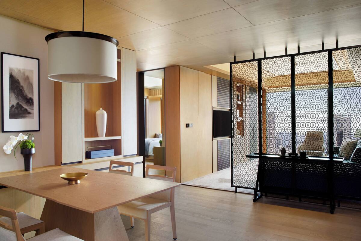 A modern interior with a wooden dining table, chairs, a large white pendant light, and a black partition with a lattice design.
