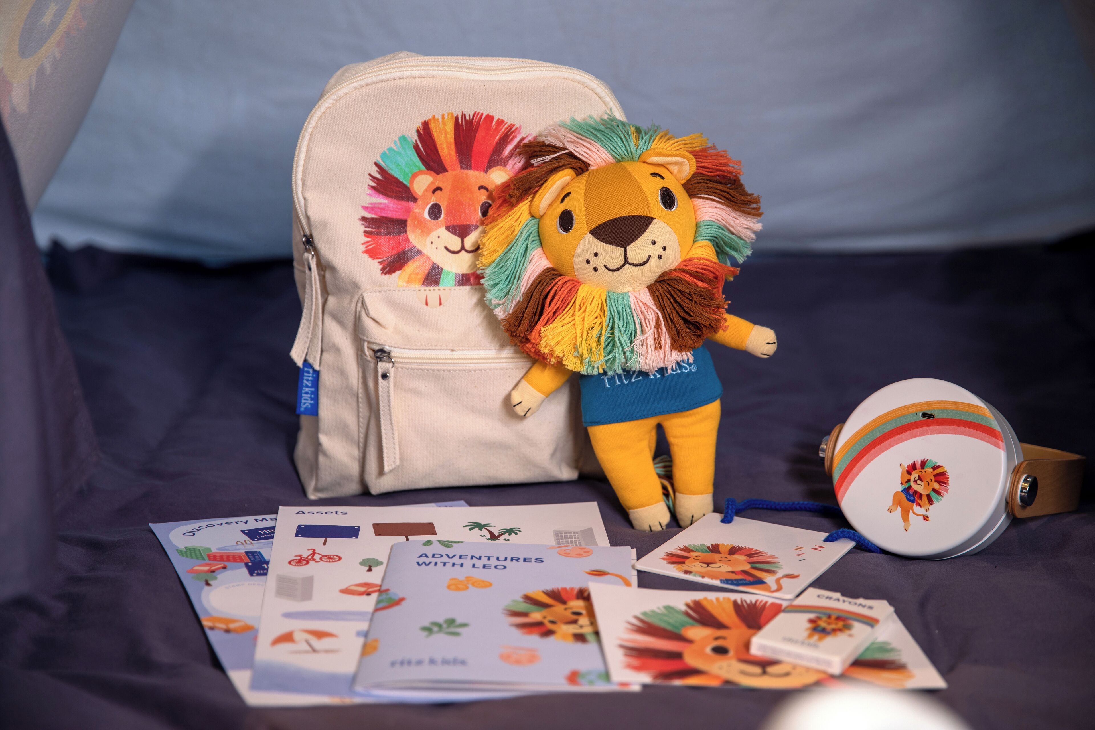 A beige backpack with a lion design, a plush toy lion, a round white object with a lion, and several cards with lion illustrations.