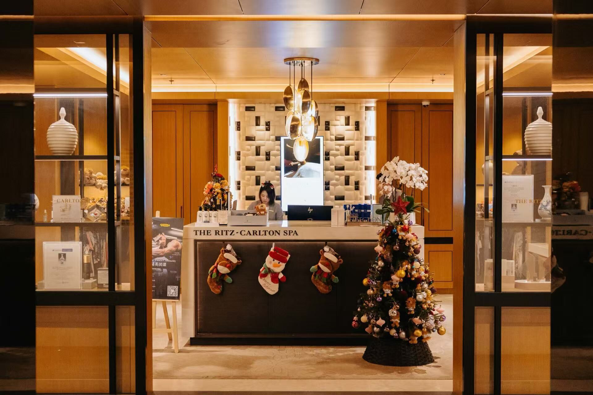 Un espace d’accueil décoré d’un sapin de Noël, avec une enseigne indiquant « Le spa du Ritz-Carlton », et une présentation de divers objets, notamment un vase et un ours en peluche.