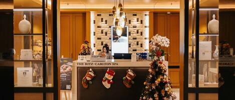 Un espace d’accueil décoré d’un sapin de Noël, avec une enseigne indiquant « Le spa du Ritz-Carlton », et une présentation de divers objets, notamment un vase et un ours en peluche.