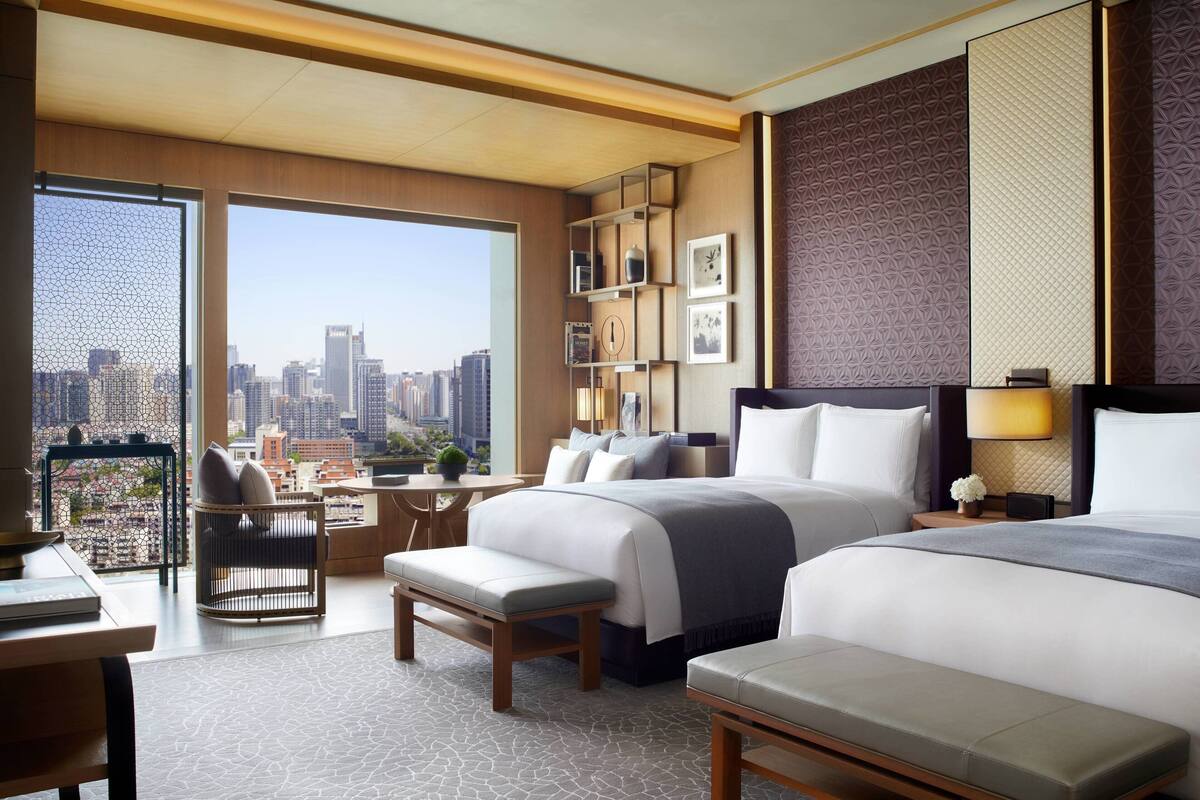 A modern hotel room with a large bed, a desk, and a view of the city skyline.