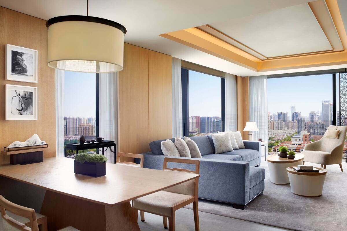 A modern living room with a sofa, chairs, a dining table, and a city view through large windows.