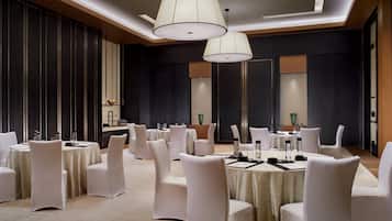 A spacious conference room with round tables, white chairs, and pendant lighting.