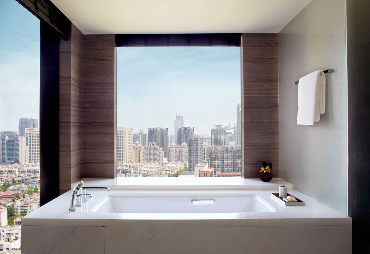 A modern bathroom with a large window, a bathtub, and a city view.