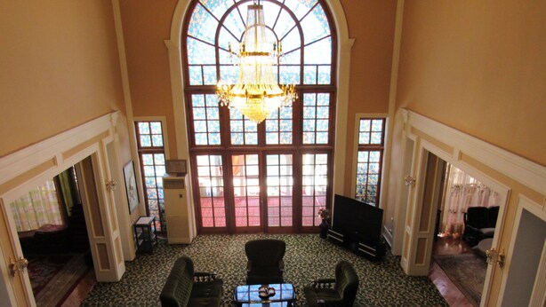Une pièce spacieuse dotée d’une grande fenêtre en arc de cercle, d’un lustre et d’un coin salon avec une table basse et des fauteuils.