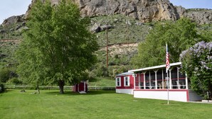 A red and white building with a flag, surrounded by green grass and trees, with a rocky mountain in the background. - Views, Central AC, Location and Solitude (Irwin)
