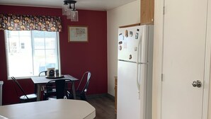 A compact kitchen with a refrigerator, a dining table with chairs, and a window with blinds. - Views, Central AC, Location and Solitude (Irwin)