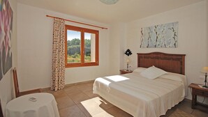 A bedroom with a large bed, a window with curtains, a bedside table with a lamp, and a painting on the wall. - Ses Rotes - Spacious country house with private pool for 10 people in Mallorca (Campanet)