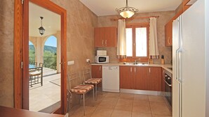 A compact kitchen with wooden cabinets, a built-in microwave, a sink, and a dishwasher. There is a dining area with a table and chairs, and a view of the outdoors through an open door. - Ses Rotes - Spacious country house with private pool for 10 people in Mallorca (Campanet)