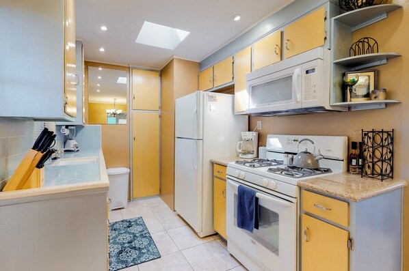 A compact kitchen with a gas stove, microwave, and a coffee maker. - The Bungalow in Downtown Joshua Tree - A Renovated Mid-Century Bungalow (Joshua Tree)