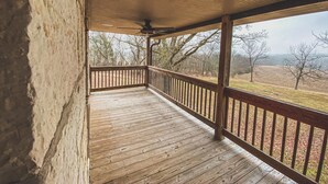 A wooden deck with a ceiling fan, overlooking a rural landscape with trees and open fields. - Funks Inn, a post civil war era home restored as it was in 1870. (Bloomsdale)