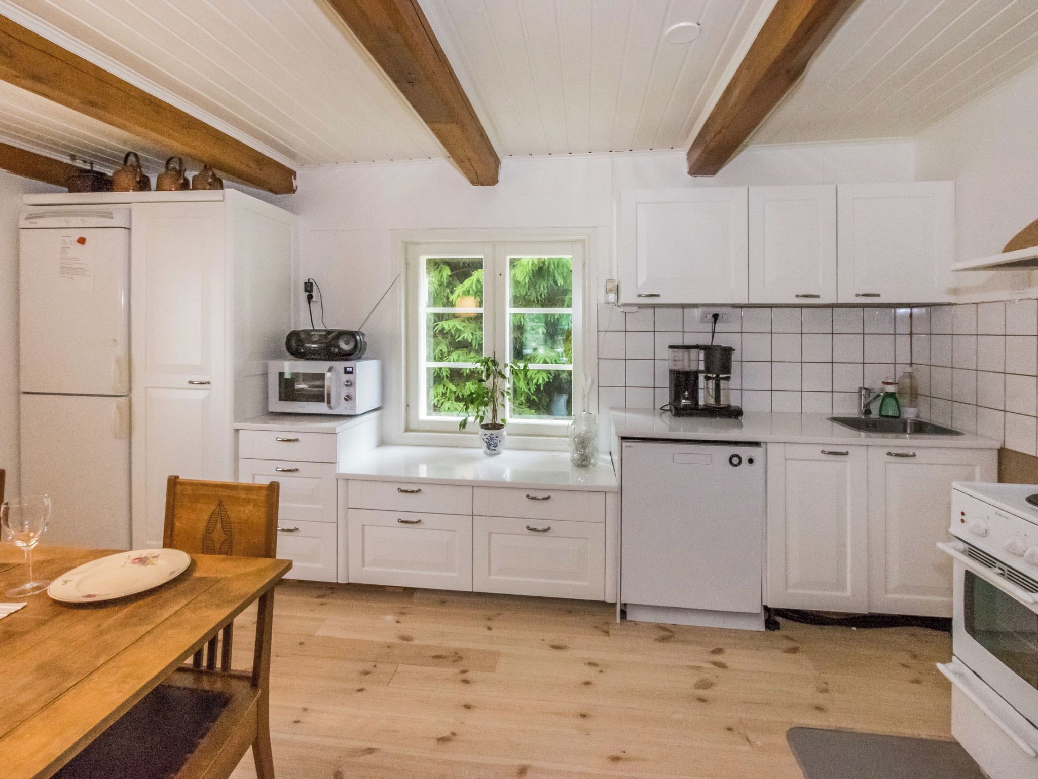 A kitchen with white cabinets, a wooden table, and a window with greenery.