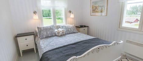 A bedroom with a bed, two bedside tables, a nightstand, a chandelier, a window with a view, and a framed picture on the wall.
