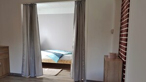 A room with a bed, wooden floor, a small wooden cabinet, and a brick wall.