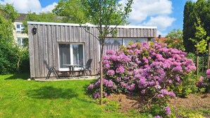 A modern wooden cabin with a patio, surrounded by a well-maintained lawn and vibrant purple flowers.