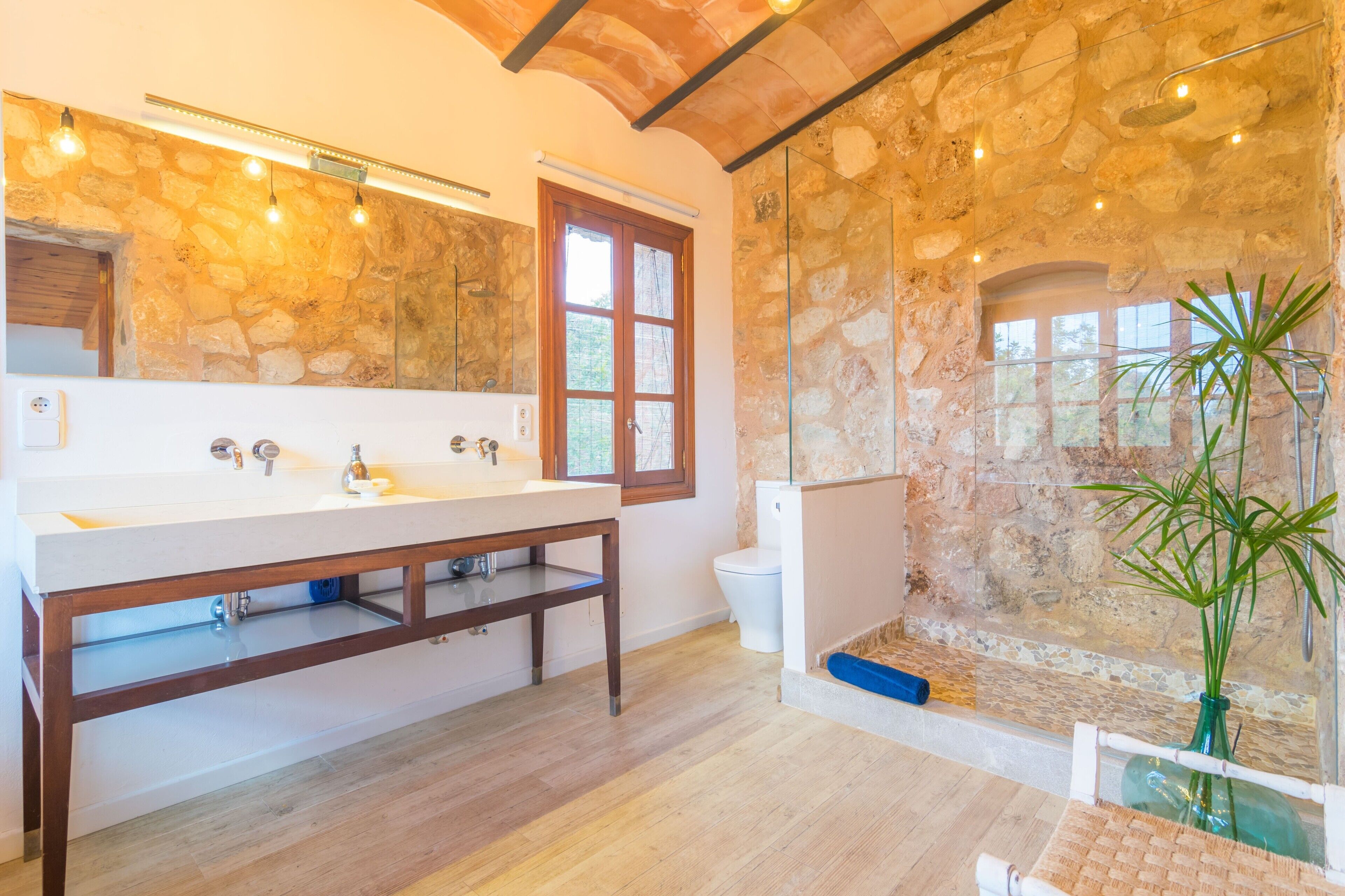 A bathroom with a stone wall, a wooden vanity, a large mirror, and a glass shower enclosure.