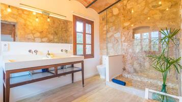 A bathroom with a stone wall, a wooden vanity, a large mirror, and a glass shower enclosure.