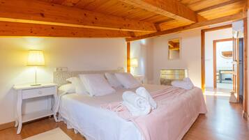 A bedroom with a wooden ceiling, a bed with white bedding, two bedside tables with lamps, and a white rug.