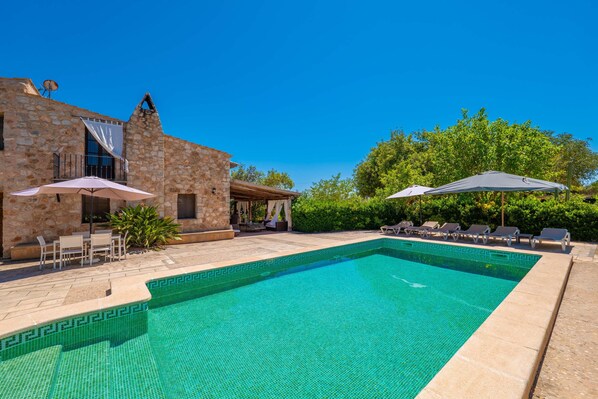 A stone building with a swimming pool, outdoor seating, and umbrellas.