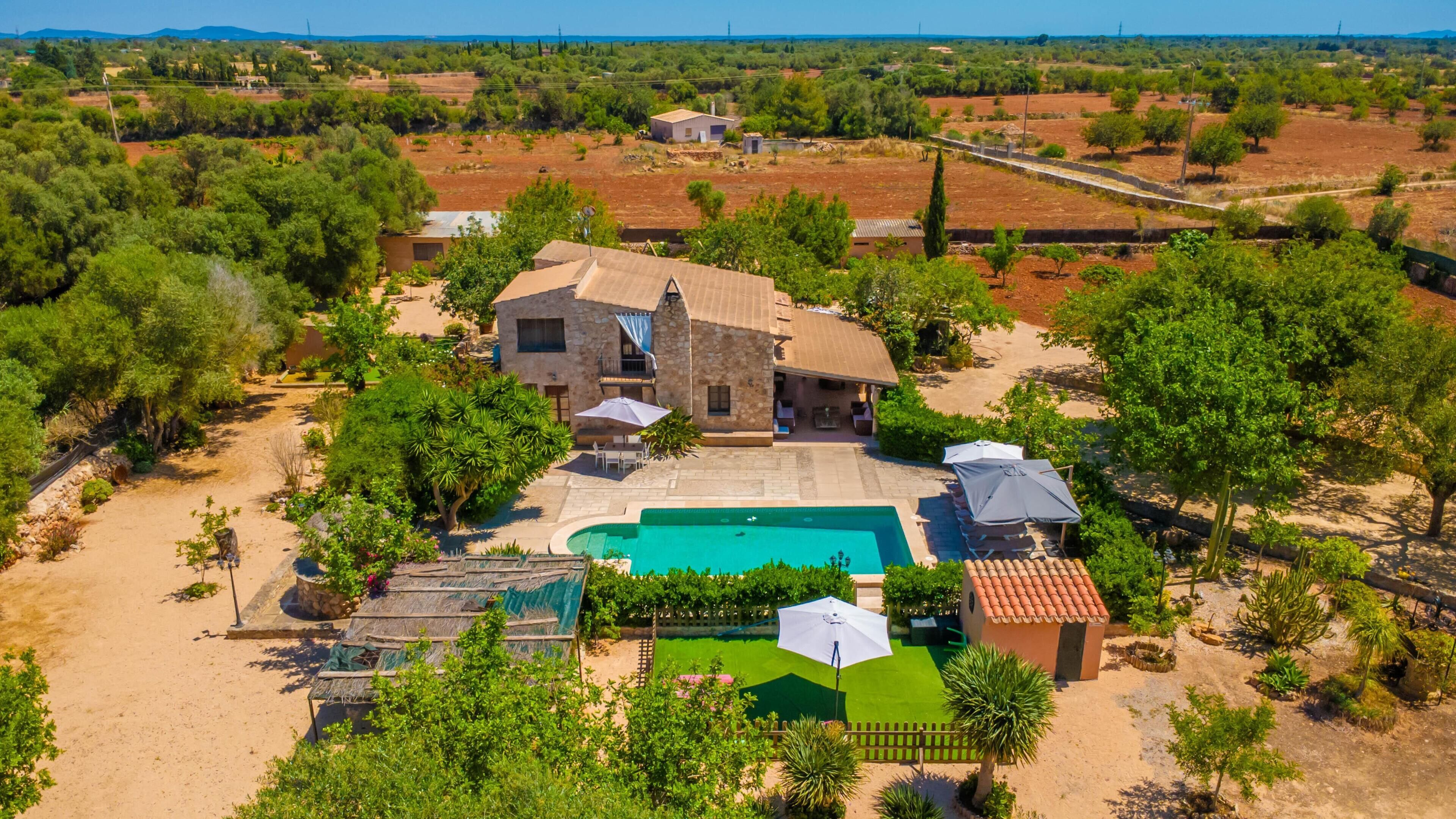 A large house with a swimming pool, surrounded by trees and open fields.
