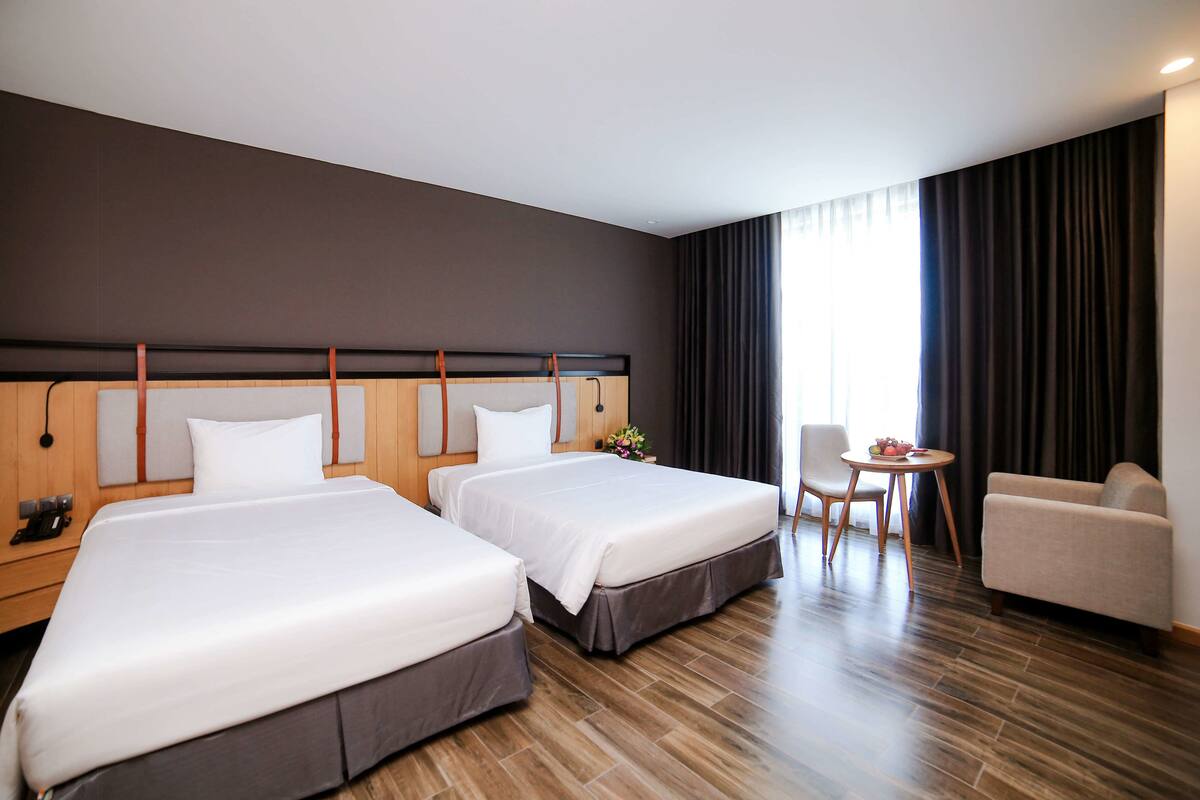 A hotel room with two beds, a sofa, a small table, and a chair.
