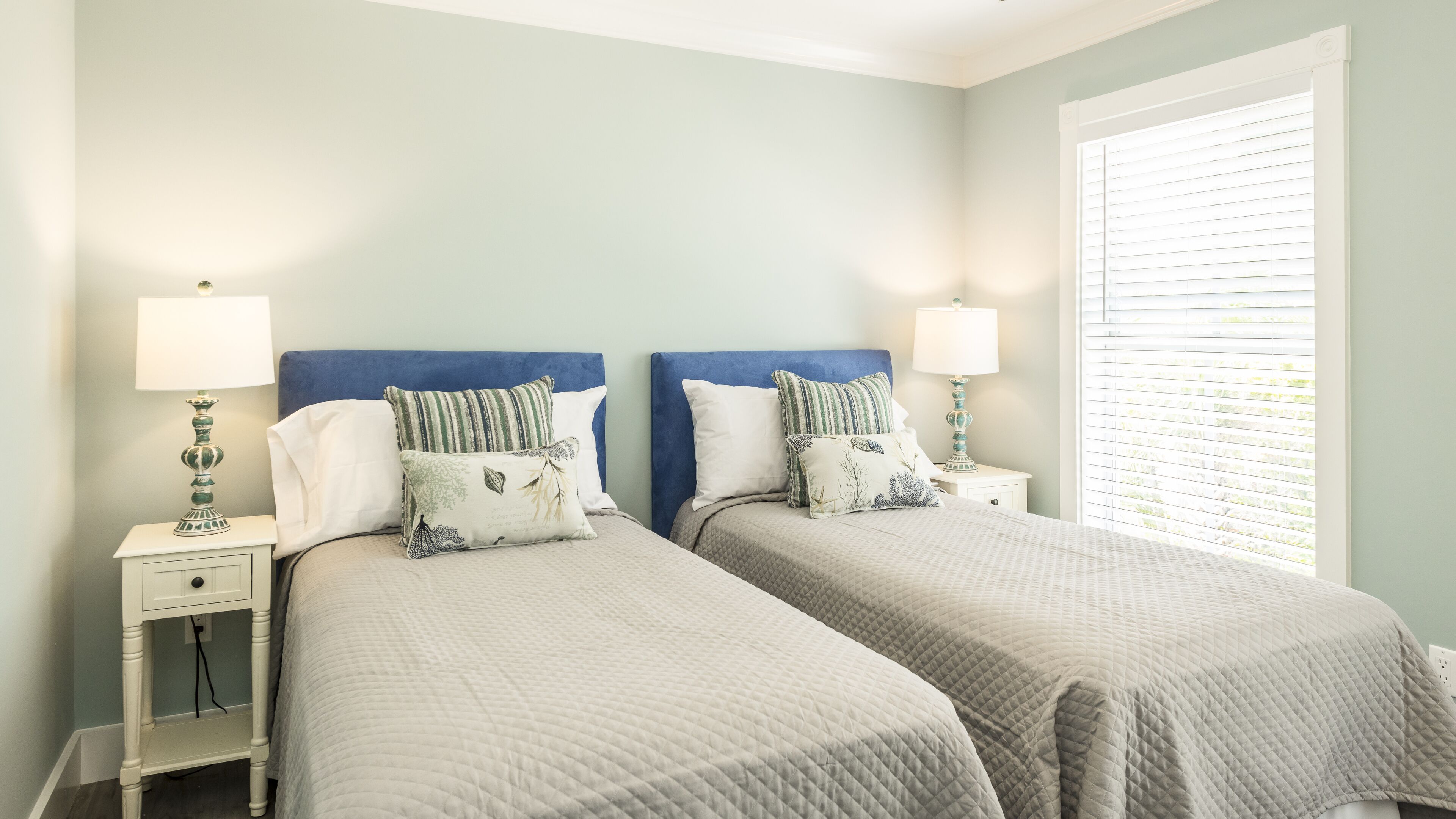 A twin bedroom with two beds, each with a blue headboard, white bedding, and matching nightstands with lamps.