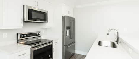 Una cocina moderna con electrodomésticos de acero inoxidable, armarios blancos y un lavamanos empotrado.