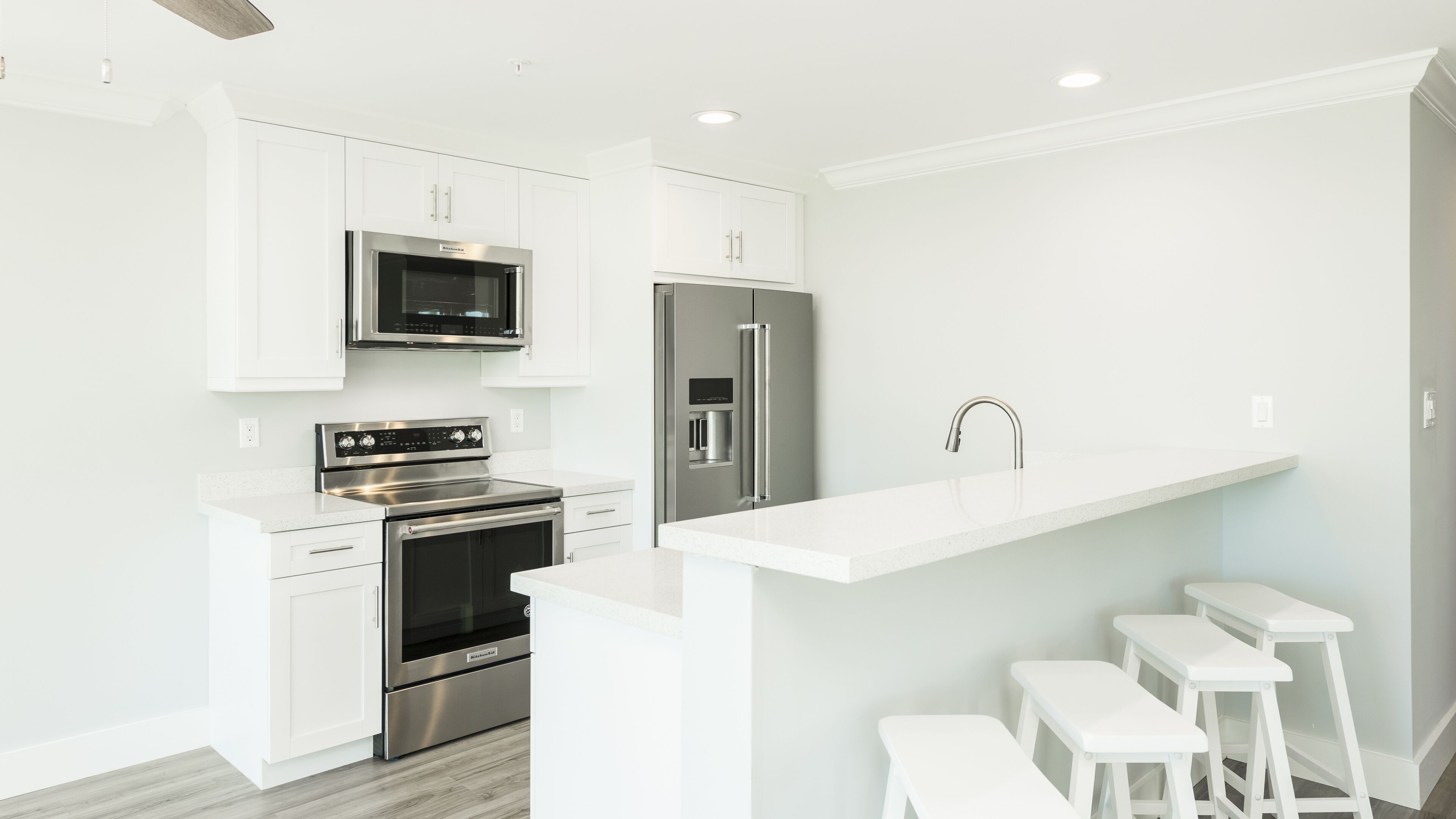 A modern kitchen with white cabinetry, stainless steel appliances, and a bar counter with stools.