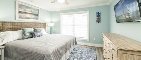 A bedroom with a bed, a ceiling fan, a window with blinds, a dresser, and a painting on the wall.