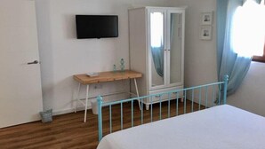 Un dormitorio con cama, armario, escritorio y televisor en la pared.