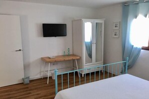 Quarto com cama, guarda-roupa, escrivaninha e televisão na parede.