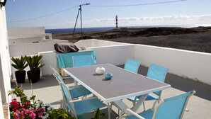 Una terraza con mesa y sillas, plantas en macetas y vistas al mar y un faro.
