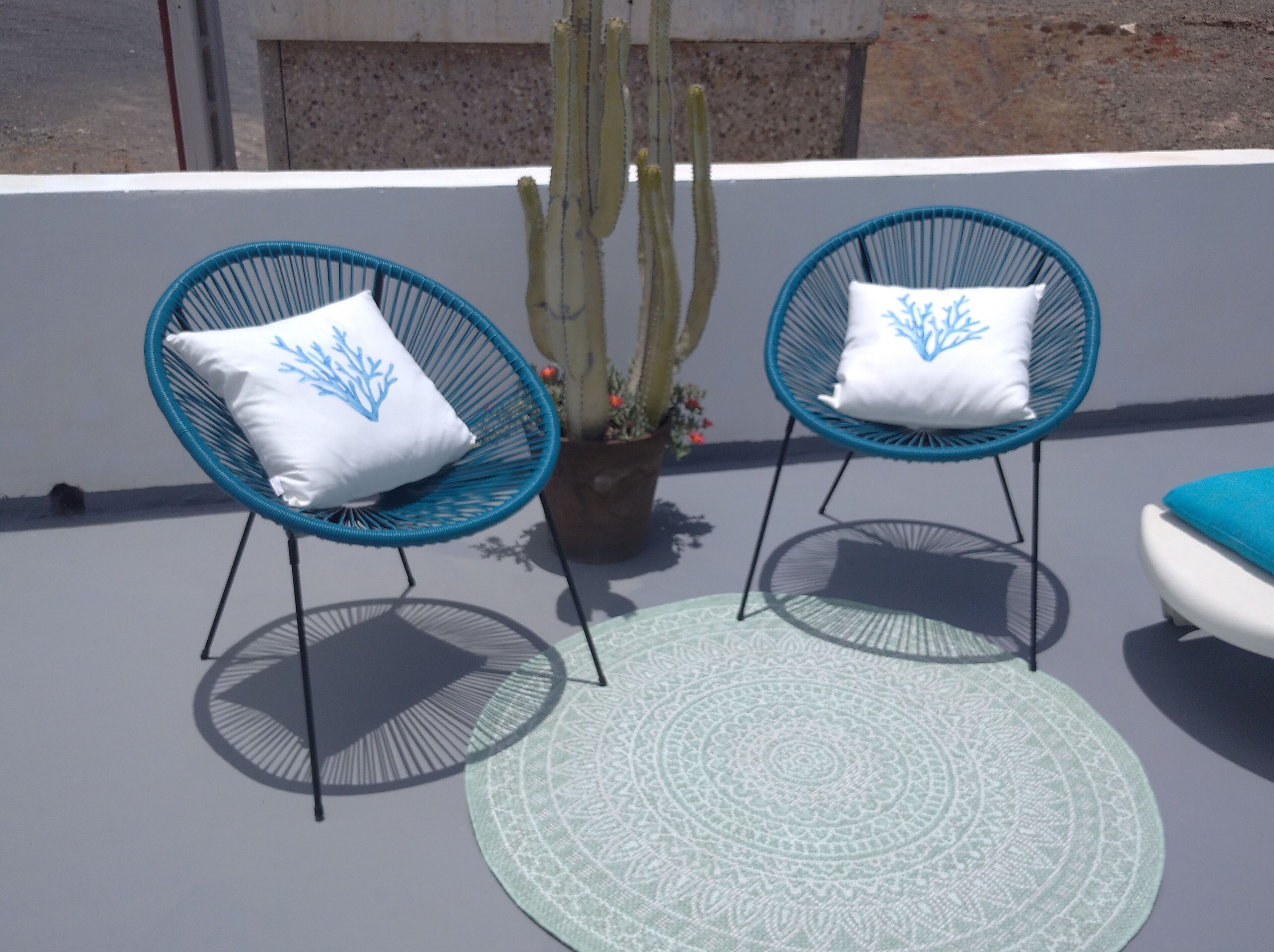Two blue chairs with white cushions and a patterned rug on a rooftop terrace.