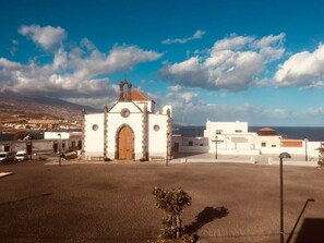 A white church with a bell tower, a paved area in front, and a view of the sea and distant buildings. - Zone 23 Home - wonderful apartment just a step away from the beach (Poris de Abona)