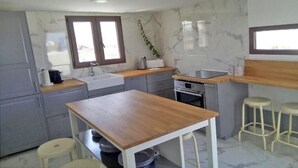 Una cocina moderna con gabinetes grises, encimera de madera, un fregadero, una estufa y dos taburetes.