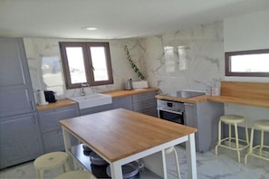 Uma cozinha moderna com armários cinzentos, bancada de madeira, pia, fogão e dois bancos.