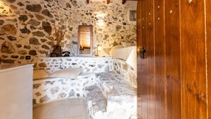 Una habitación con paredes de piedra, una puerta de madera, una cama y una pequeña mesa con lámpara.