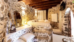 Un dormitorio con paredes de piedra y techo de madera, una cama, una mesita de noche y un espejo.
