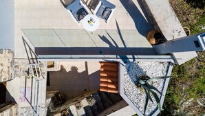 Vista aérea de una terraza en la azotea con una mesa de vidrio, dos sillas y una pequeña planta en maceta.