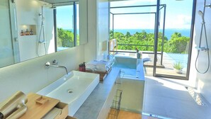 Une salle de bain moderne dotée d’une grande baignoire, d’une douche à l’italienne et d’un espace de douche vitré offrant une vue sur l’océan.