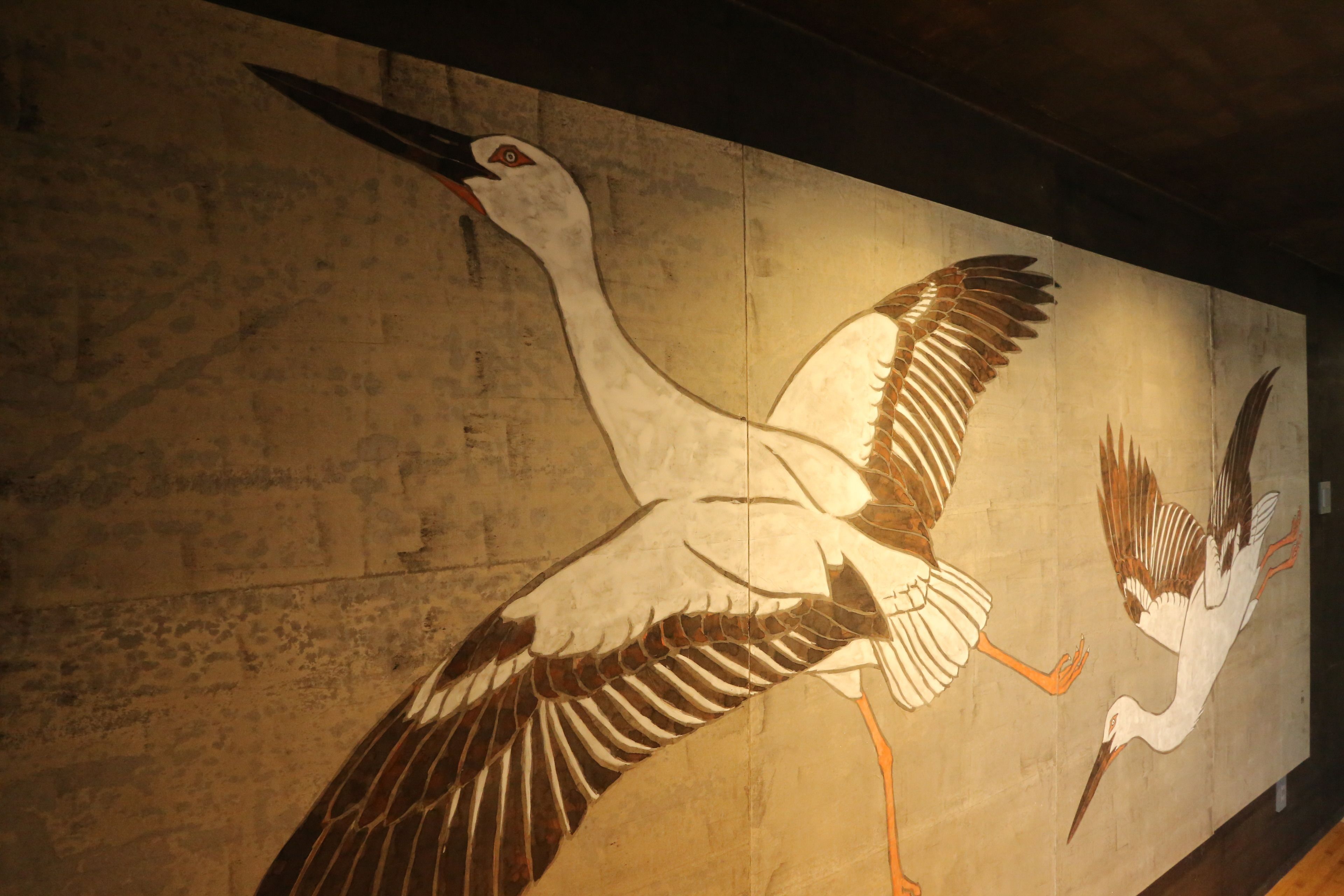 Un mural de dos grullas volando sobre una pared con textura.