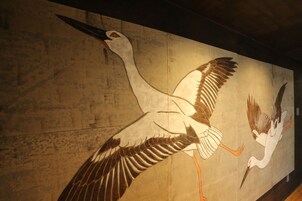 Un mural de dos grullas volando sobre una pared con textura.