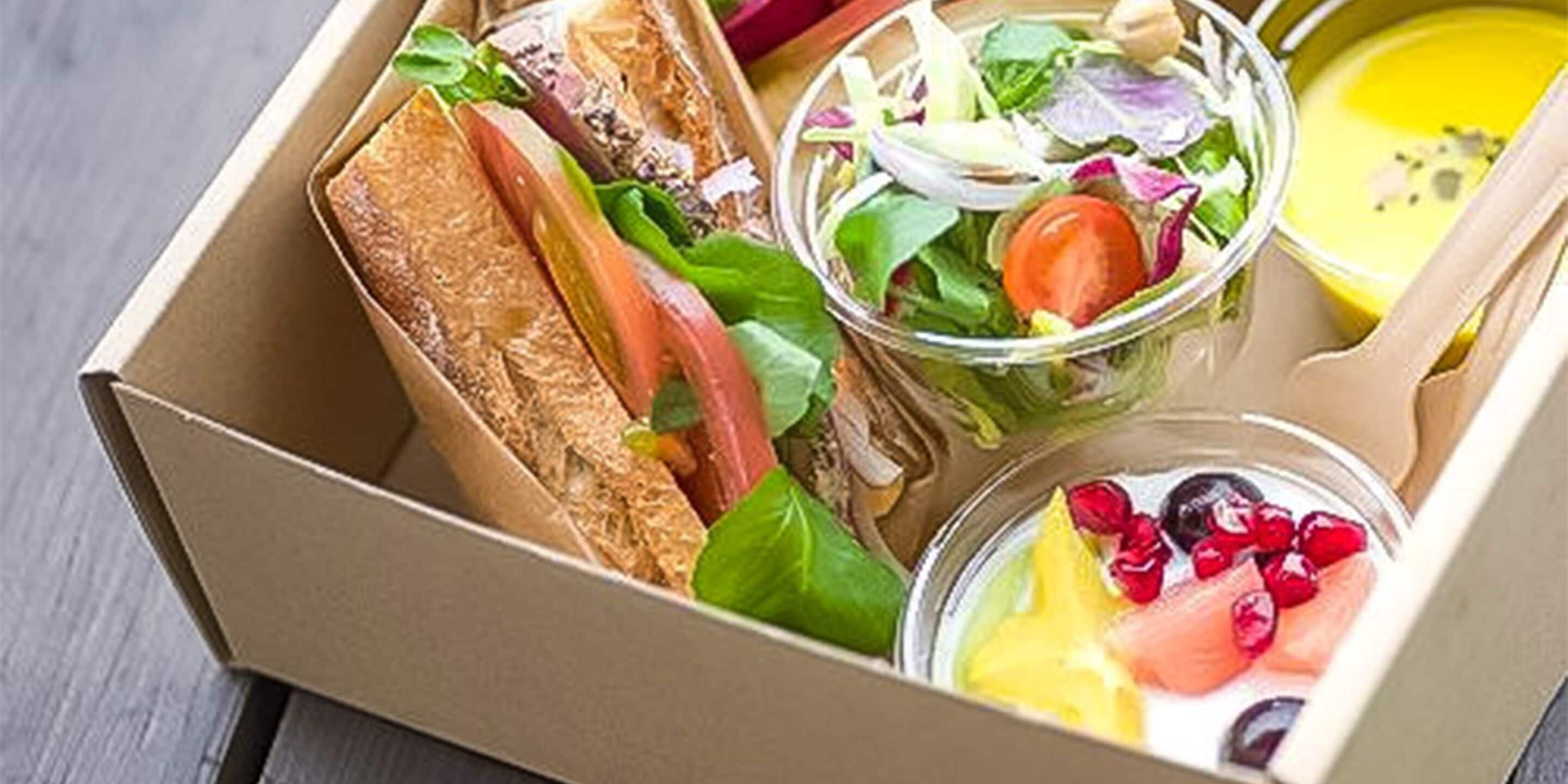 A lunchbox containing sandwiches, a salad, a bowl of soup, and a fruit cup.